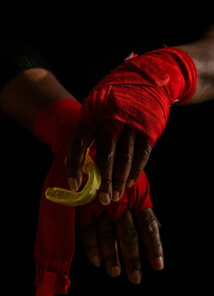 Boxer wearing red wraps holding a yellow sports mouthguard – promoting dental protection for athletes