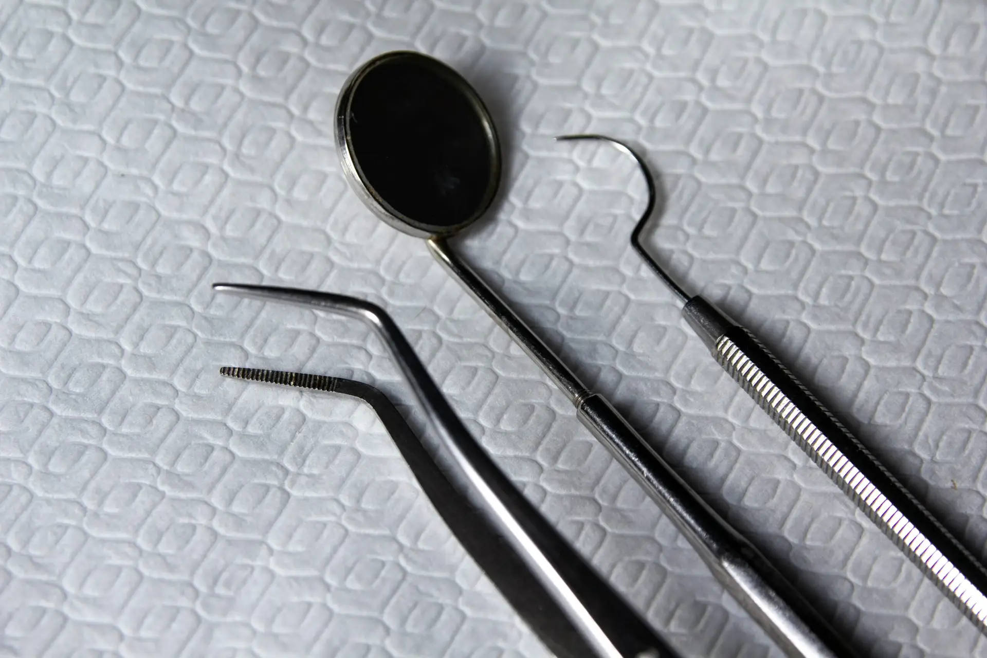 Close-up of dental tools on a textured clinical surface, including a mirror, dental probe, and tweezers, symbolizing dental care and patient experience.