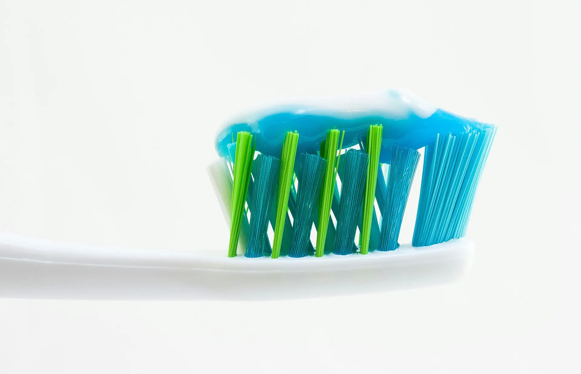 Close-up of a toothbrush with blue and green bristles and a stripe of blue toothpaste, symbolising daily oral care